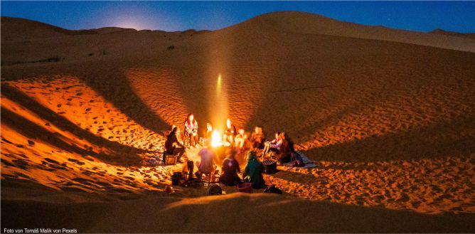 Freunde im Kreis um ein Lagerfeuer in der Wüste.