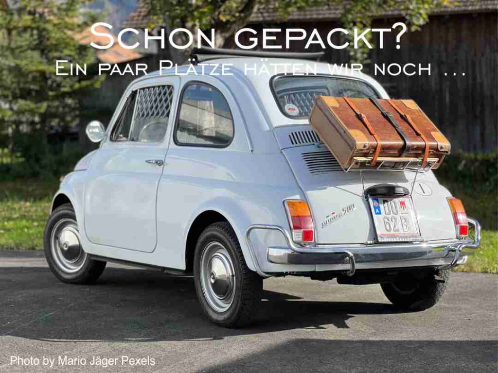 kleiner weißer alter Fiat mit hinten aufgebundenen Lederkoffer